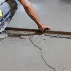 Obrero con botas y cinta métrica trabajando en como nivelar un suelo de cemento con una regla de albañil.