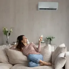 Mujer sonríe en el sofá, disfrutando de la temperatura ideal del aire acondicionado.