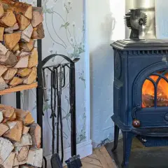 Estufa de leña con fuego encendido y leña apilada. Un ventilador para estufa de leña opiniones positivas sobre su eficiencia.