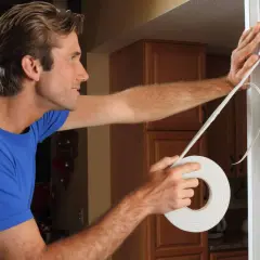 Hombre con camiseta azul aplica cinta para tapar hueco en puerta de entrada.