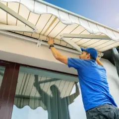 Hombre con gorra azul trabajando en la instalación o reparación de un toldo, ajustando la tela.