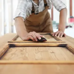 Carpintero lijando una puerta de sapelly para modernizarla, revelando la veta de la madera.