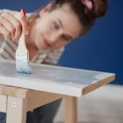 Mujer pintando muebles de melamina con brocha y pintura azul claro.