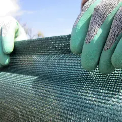 Manos enguantadas sujetan malla verde, buscando ideas ocultación jardín para crear privacidad y sombra.