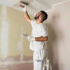 Hombre enmasillando techo y pared. Presupuesto para pintar piso.