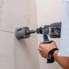 Un hombre usa un taladro con corona para hacer un agujero en una pared de hormigón. Se puede taladrar una viga de hormigón con esta herramienta.