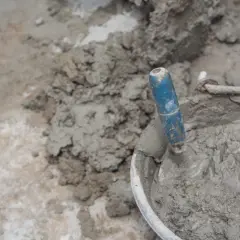 Paleta azul en un cubo con cemento fresco. El proceso de cómo hacer cemento es fundamental para la construcción.