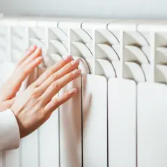 Manos tocando un radiador blanco. Aprende cómo limpiar radiadores para un hogar cálido y eficiente.