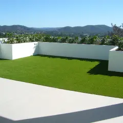 Terraza con césped artificial verde brillante y vistas a montañas. Podría haber inconvenientes de poner césped artificial en terraza, como el calor.