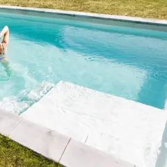 Mujer en bikini azul disfruta de su piscina cristalina, demostrando la facilidad de limpiar piscina sin vaciar agua.