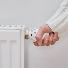 Mano ajustando el termostato de un radiador blanco. Parece que el radiador no calienta, a pesar de los ajustes.