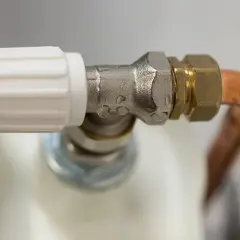 Detalle de una llave de radiador que gotea, con gotas de agua visibles en la conexión metálica.