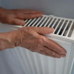 Manos sobre un radiador blanco, sintiendo el calor. ¿Por qué suenan los radiadores?