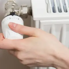 Mano ajustando el termostato de un radiador. Gira la perilla para abrir el radiador derecha o izquierda, regulando la temperatura.