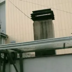 La chimenea del vecino desprende humo que me entra. Se ven varias chimeneas y tuberías en un tejado.