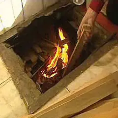 Manos añaden leña a un fuego en un hogar, brindando **gloria calefacción** a la estancia.