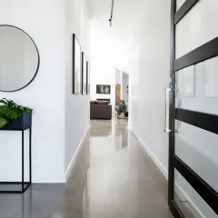 Pasillo moderno con suelo resina epoxi vivienda, espejo redondo, planta y puerta de cristal.