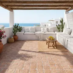 Terraza mediterránea con suelo de baldosas de terracota, sofás blancos, cactus y flores. Cumple la norma resbaladicidad c1, c2, c3.