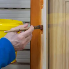 Persona aplica barniz a una puerta de madera con un pincel. El proceso de lacar puertas protege y embellece la madera.