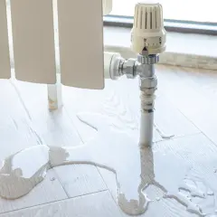 Fuga de agua en el suelo de madera cerca de un radiador. El agua se acumula, indicando la necesidad de quitar un radiador definitivamente.