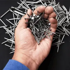 Una mano sostiene un montón de clavos, mostrando varios tipos de clavos sobre un fondo oscuro.