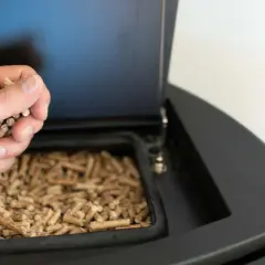 Mano añadiendo pellets a una estufa de leña. Preparando la instalación de estufa pellets para un invierno cálido.
