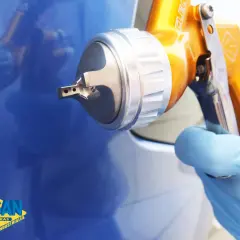 Persona con guante azul usa pistola para pintar paredes de azul brillante.