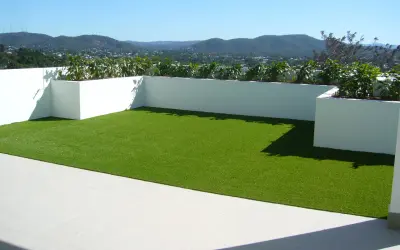 Terraza con césped artificial verde brillante y vistas a montañas. Podría haber inconvenientes de poner césped artificial en terraza, como el calor.