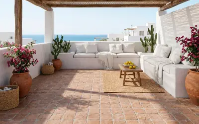 Terraza mediterránea con suelo de baldosas de terracota, sofás blancos, cactus y flores. Cumple la norma resbaladicidad c1, c2, c3.