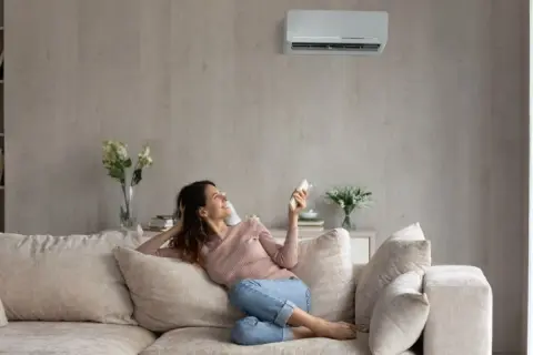 Mujer sonríe en el sofá, disfrutando de la temperatura ideal del aire acondicionado.