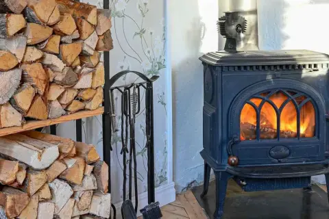 Estufa de leña con fuego encendido y leña apilada. Un ventilador para estufa de leña opiniones positivas sobre su eficiencia.