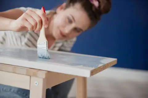 Mujer pintando muebles de melamina con brocha y pintura azul claro.