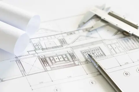 Plano arquitectónico con un **muro de carga** detallado. Se observan rollos de papel, un calibrador y un bolígrafo, listos para el diseño.