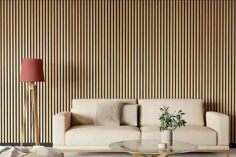 Una pared con listones de madera verticales, ideal para quienes buscan ideas sobre como poner listones de madera en la pared. Un sofá beige y una lámpara roja completan la escena.