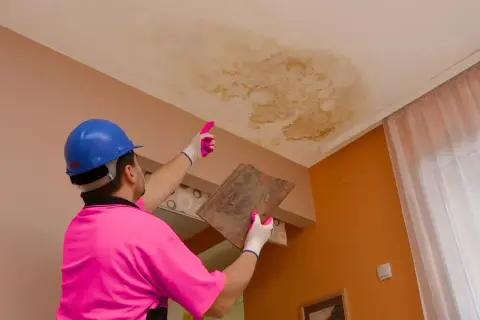Un trabajador con casco azul y polo rosa señala una mancha de humedad en el techo, indicando que se puede caer el techo por una gotera.