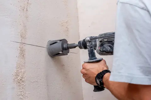 Un hombre usa un taladro con corona para hacer un agujero en una pared de hormigón. Se puede taladrar una viga de hormigón con esta herramienta.