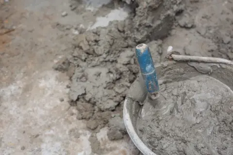 Paleta azul en un cubo con cemento fresco. El proceso de cómo hacer cemento es fundamental para la construcción.