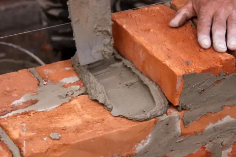 Mano coloca ladrillo sobre mortero fresco. Aprende como hacer mortero para construir.