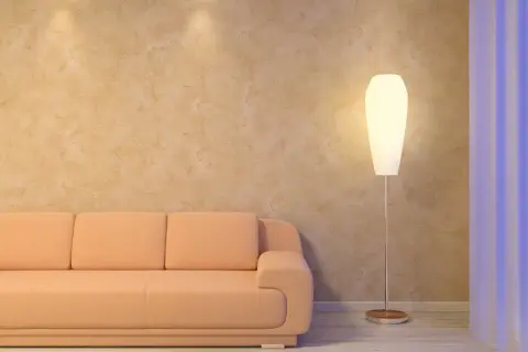 Sofá naranja junto a una lámpara de pie, con una pared texturizada que parece estucar una pared con un acabado rústico.