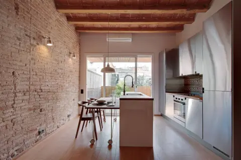Cocina moderna con pared de ladrillo visto y pintura efecto envejecido. Vigas de madera en el techo y suelo de parqué.