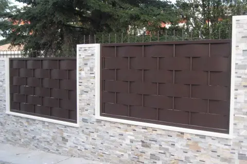 Muro de piedra con paneles de valla de metal marrón oscuro, un ejemplo de tipos de vallas para chalet.