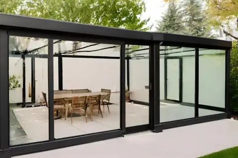 Modernos tipos de cerramientos de cristal con mesa y sillas en el interior, creando un espacio elegante y luminoso.