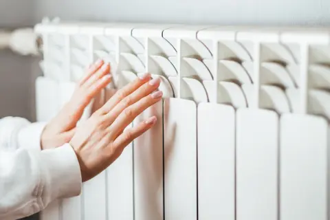 Manos tocando un radiador blanco. Aprende cómo limpiar radiadores para un hogar cálido y eficiente.