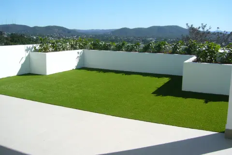 Terraza con césped artificial verde brillante y vistas a montañas. Podría haber inconvenientes de poner césped artificial en terraza, como el calor.