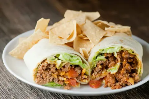Un taco quimico como funciona: carne molida, lechuga, tomate y queso envueltos en tortilla, servido con totopos.