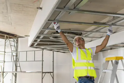 Obrero mide estructura de techo falso. Para saber si un muro es de carga, observa su grosor y si soporta peso.