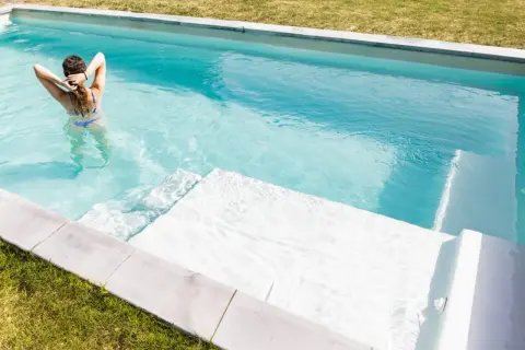 Mujer en bikini azul disfruta de su piscina cristalina, demostrando la facilidad de limpiar piscina sin vaciar agua.