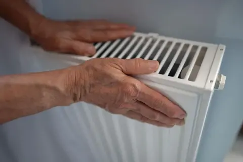 Manos sobre un radiador blanco, sintiendo el calor. ¿Por qué suenan los radiadores?