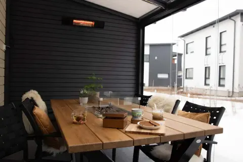 Mesa de madera en terraza cerrada con calefactor, ideal para disfrutar del exterior incluso con nieve.