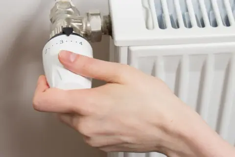 Mano ajustando el termostato de un radiador. Gira la perilla para abrir el radiador derecha o izquierda, regulando la temperatura.